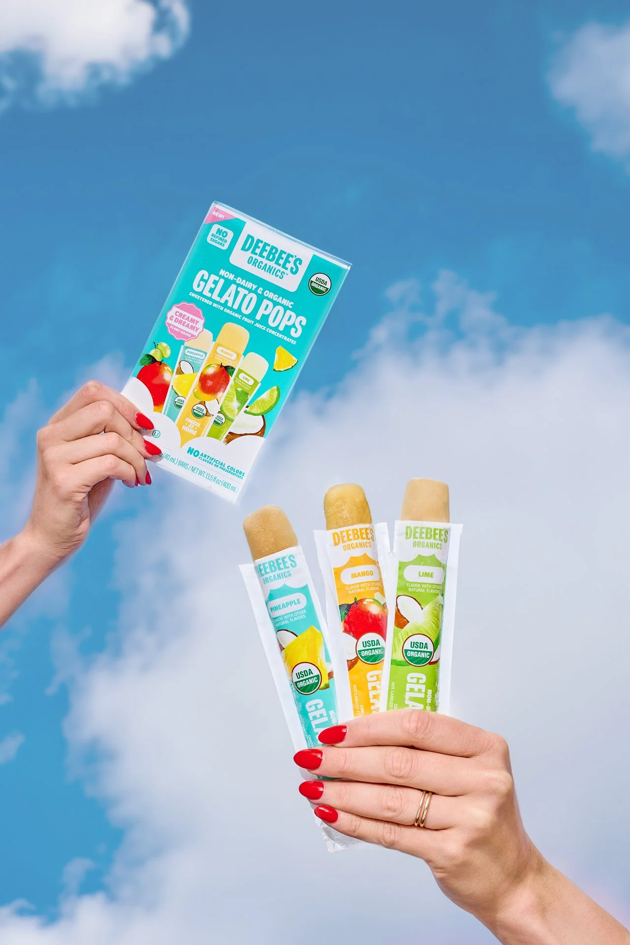 two hands holding a box of frozen treats and opened freezies against a blue sky