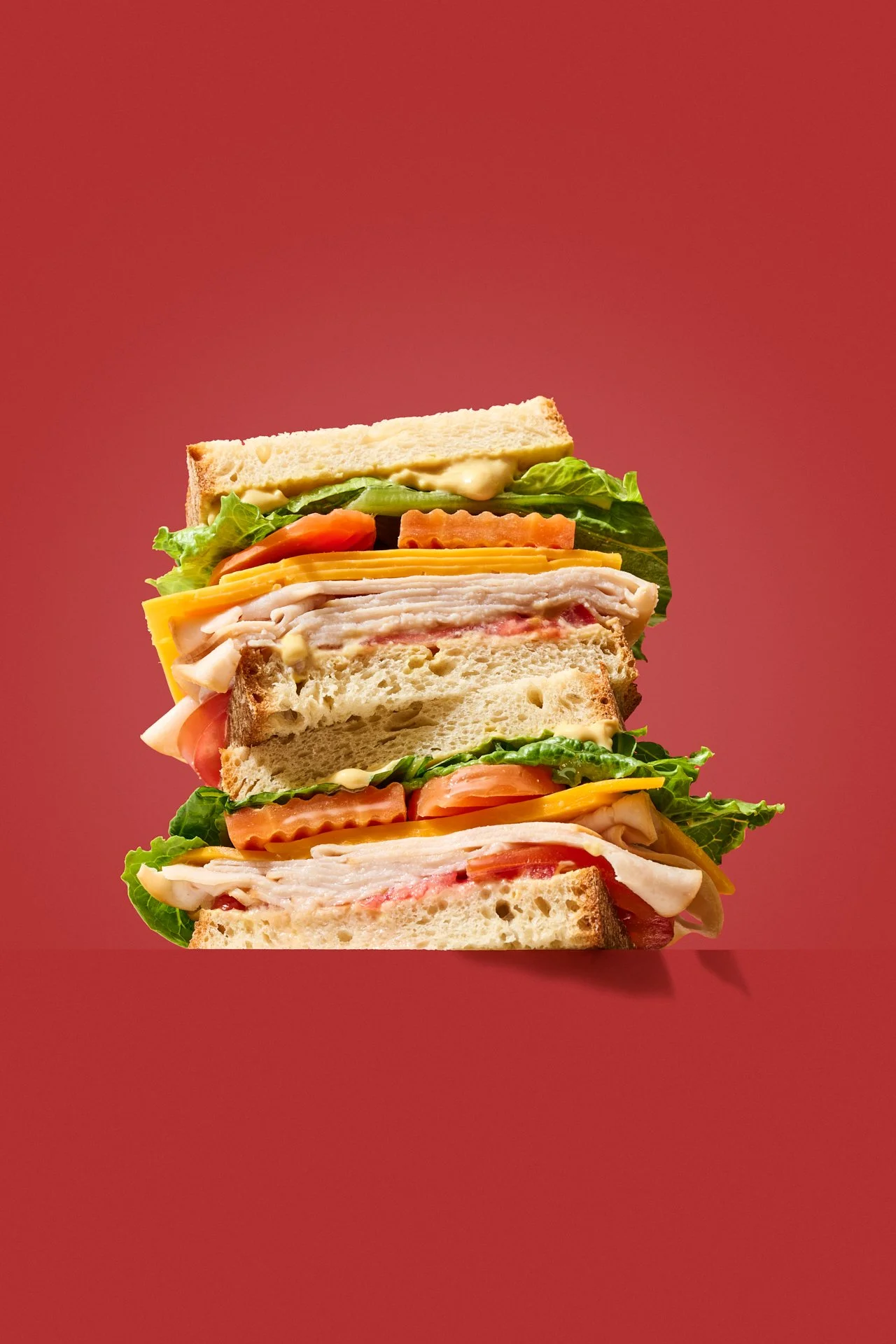 pointing up at a hero sandwich with carrots, lettuce, sliced meat and tomato against a red background