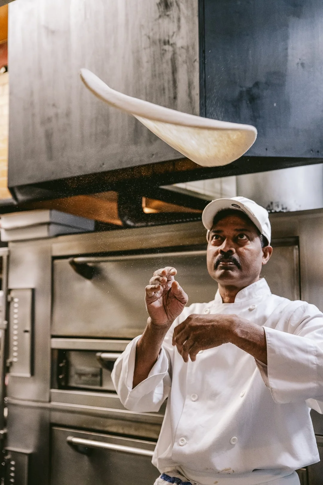 a chef slinging a pizza in the restaurant kitchen