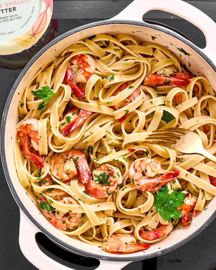 a stop motion of a white enamel pot filled with shrimp linguine and green parsley, a fork twirls the pasta and brings it out of the frame. churn's garlic and shallot butter is in the frame