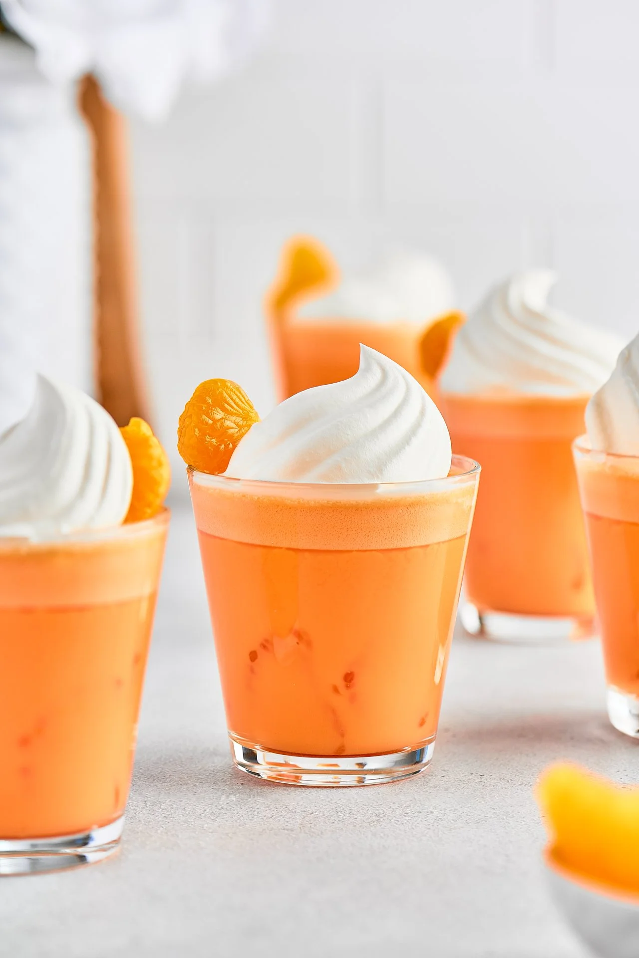 Close-up of orange-colored dessert with dollops of whipped cream and a small mandarin orange slice on top, in a clear glass.