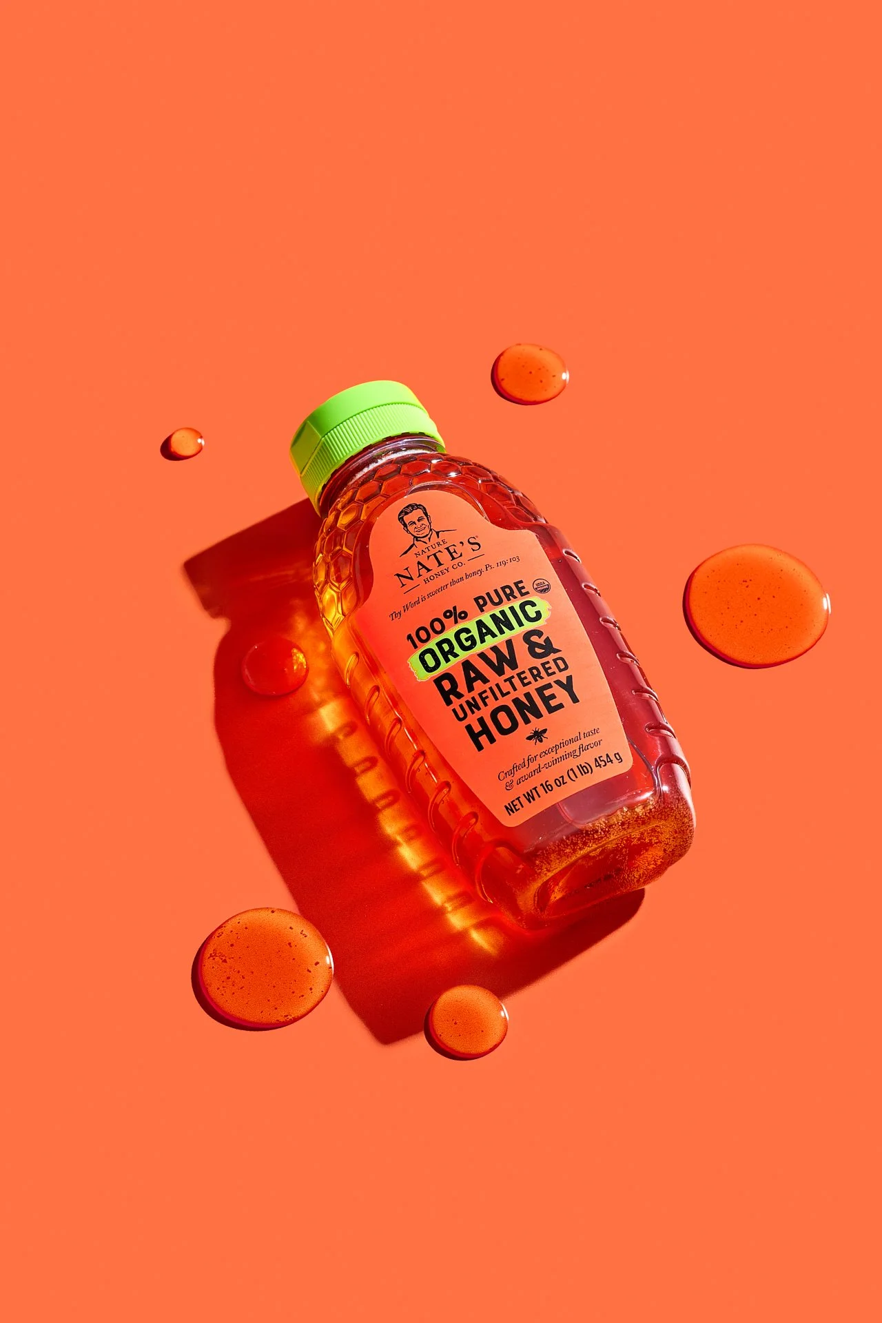 bold, colorful, vibrant commercial product photography in a production studio of a nate's honey bottle surrounded by honey droplets on a bright orange background.
