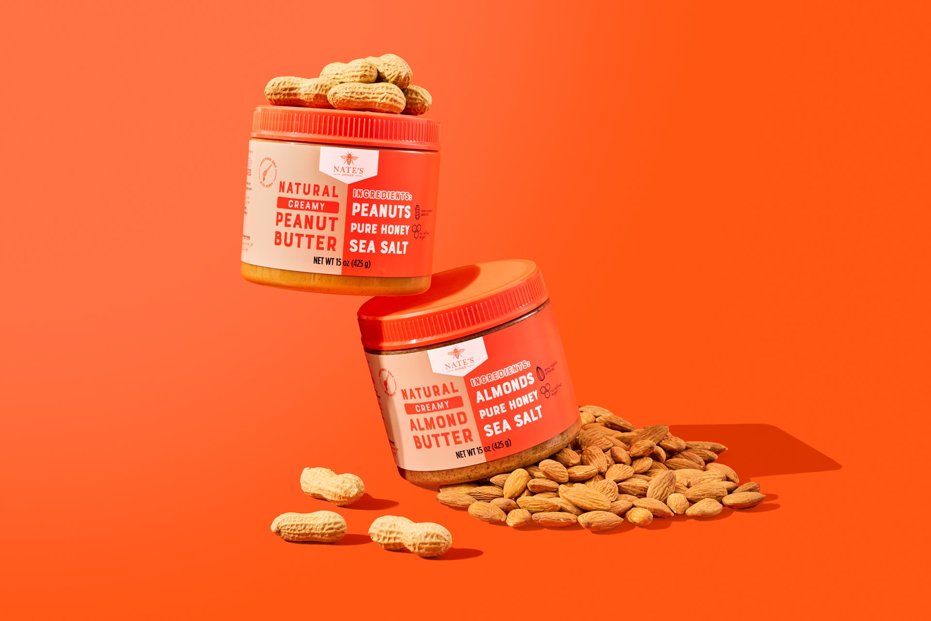 product image of nate's peanut and almond butter resting on a pile of almonds on a solid orange background