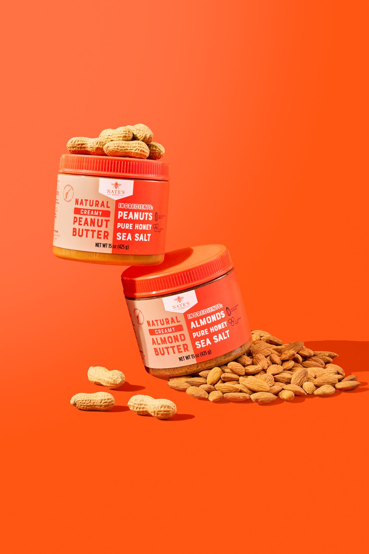 Commercial food photography of nut butter spread jars styled with peanuts and almond ingredients on a bright orange set.
