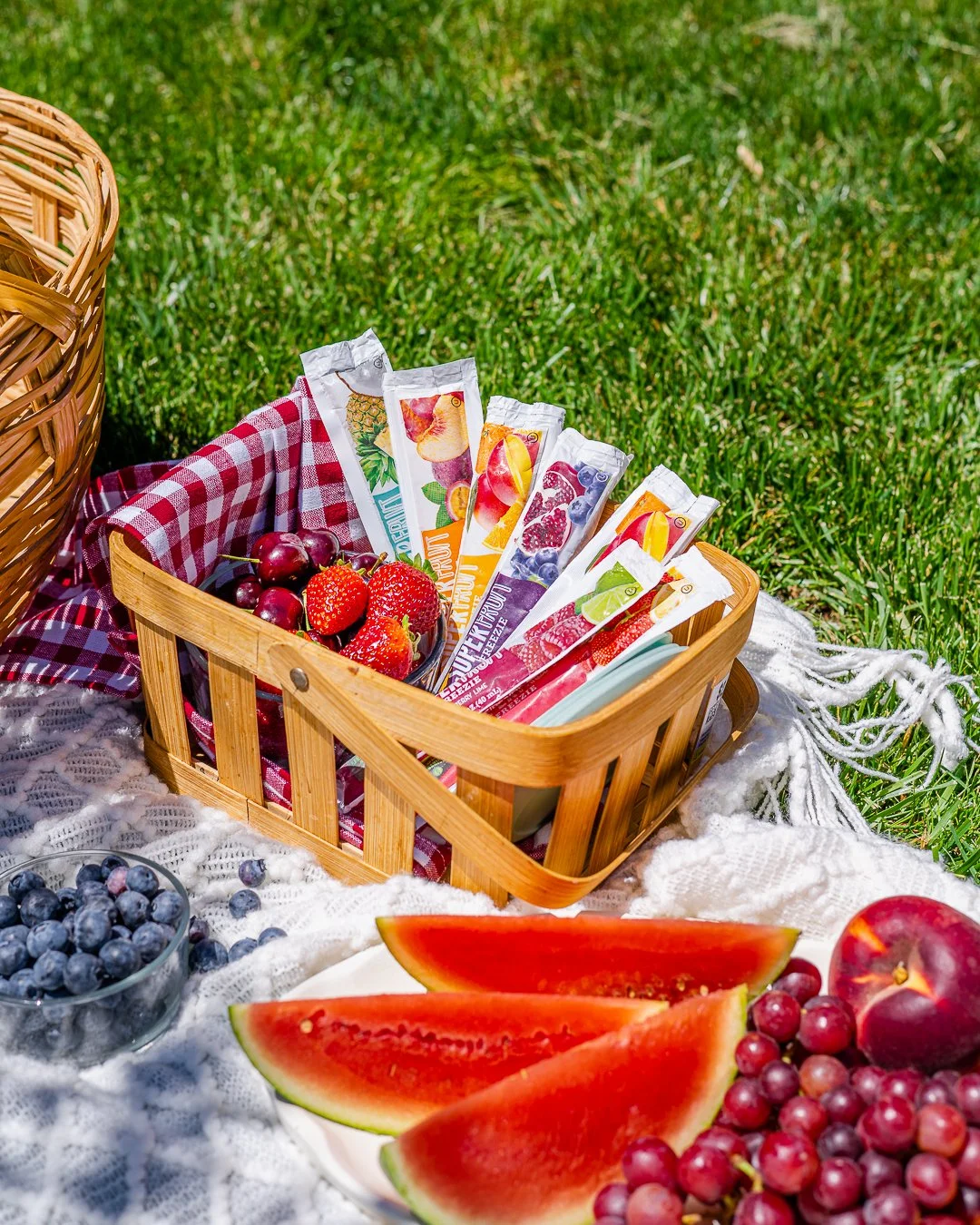 a basket with freezies and fresh fruits in it in a picnic setting