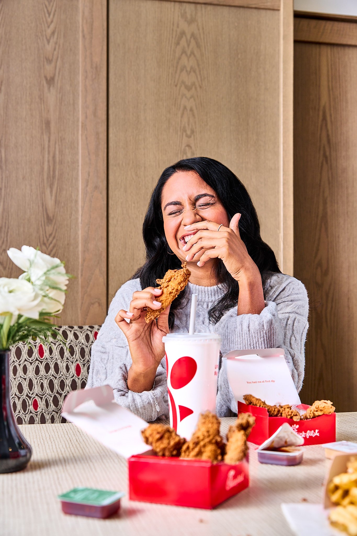 a women smiling and laughing eating her chick-fil-a chicken tender and fries on the restaurant