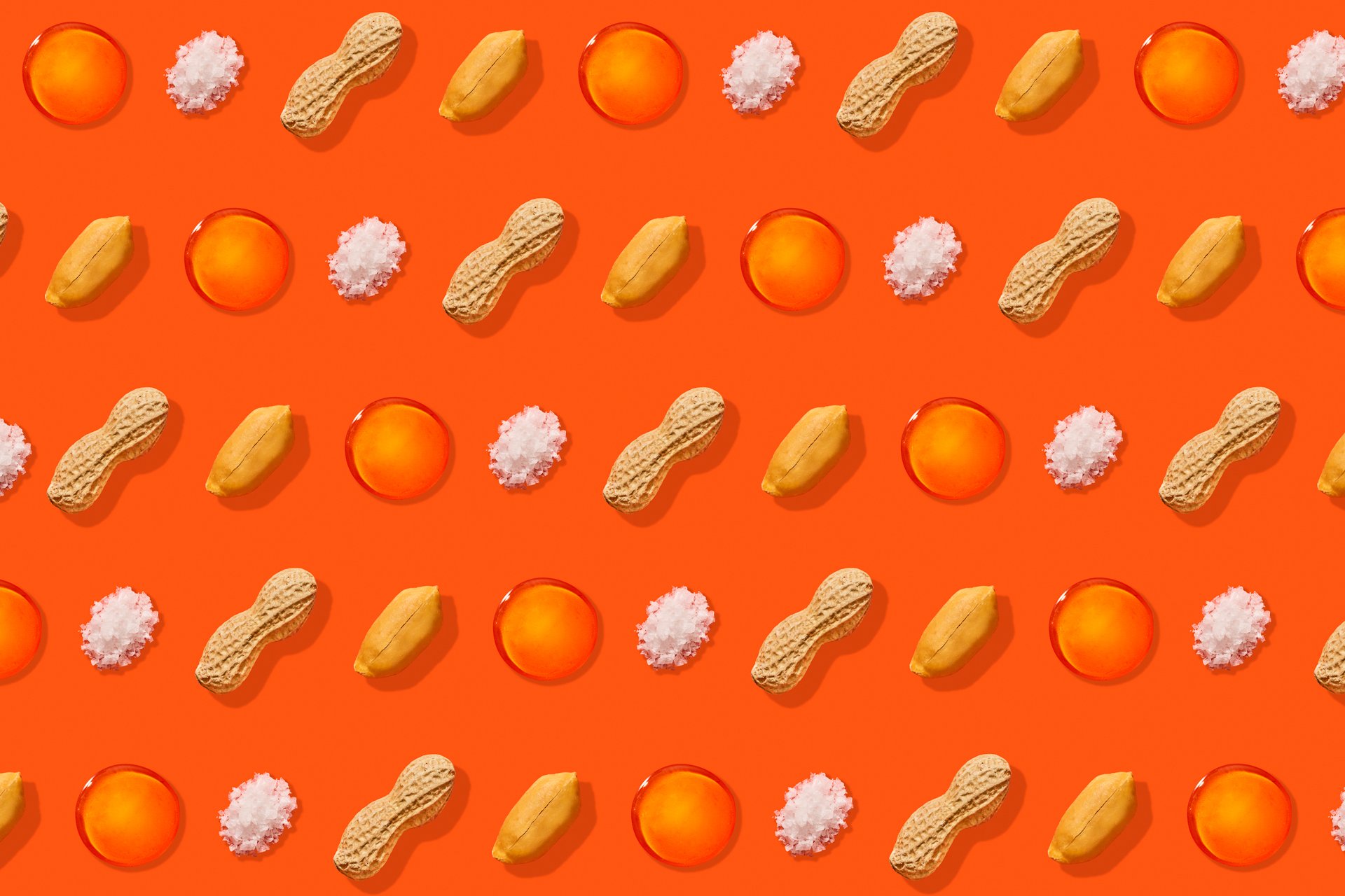 Repeating pattern of loose handfuls of salt, spilled peanuts, orange capsules, and yellow lemons on an orange background.