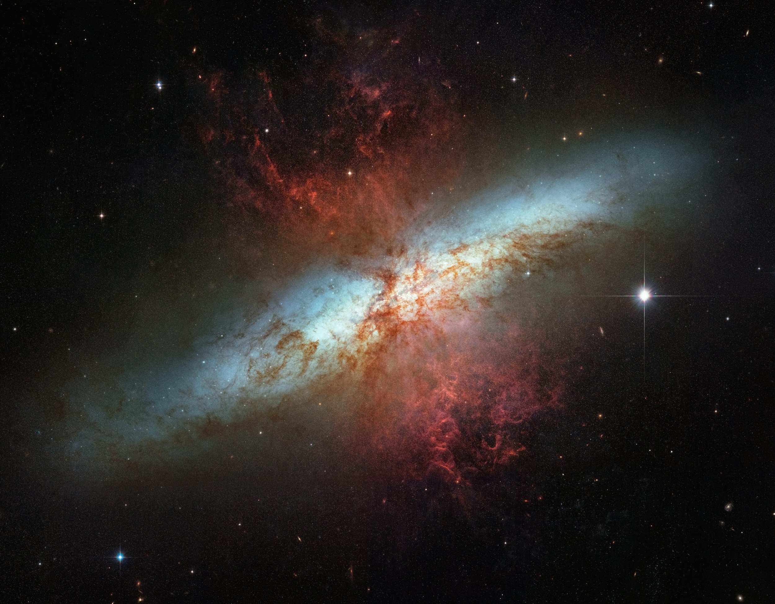 A colorful galaxy with bright blue, red, and white regions, surrounded by numerous stars and cosmic dust in space.