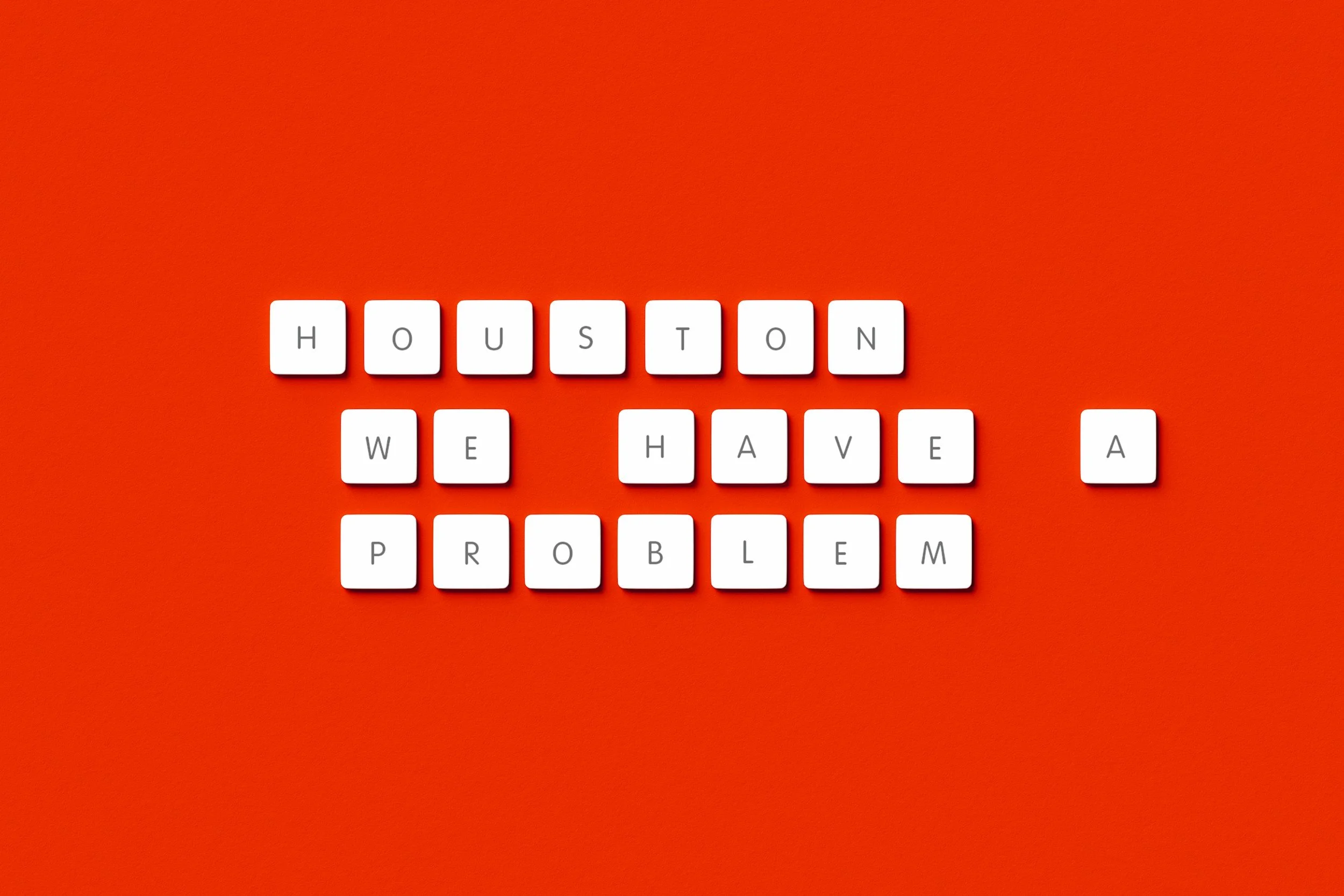 Letter tiles spelling out 'HOUSTON WE HAVE A PROBLEM' on an orange background.