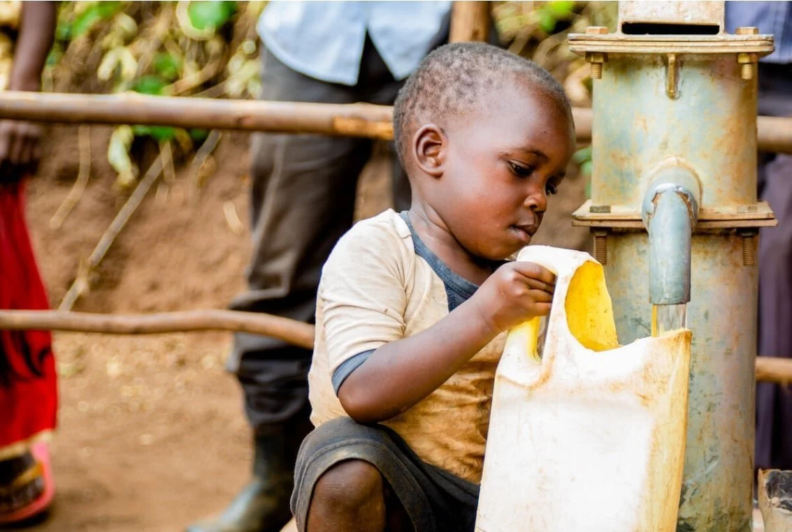 Child filling a container with water from a hand pump.