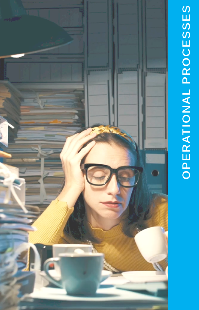 Lady wearing a yellow sweater in glasses leaning over on a desk looking exhausted with piles of paper all around