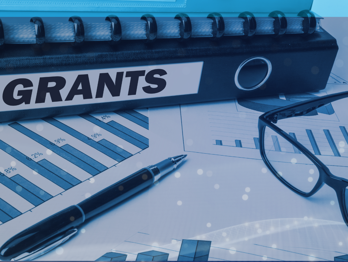 Binder with wording grants on top of charts with a pen and glasses next to the charts