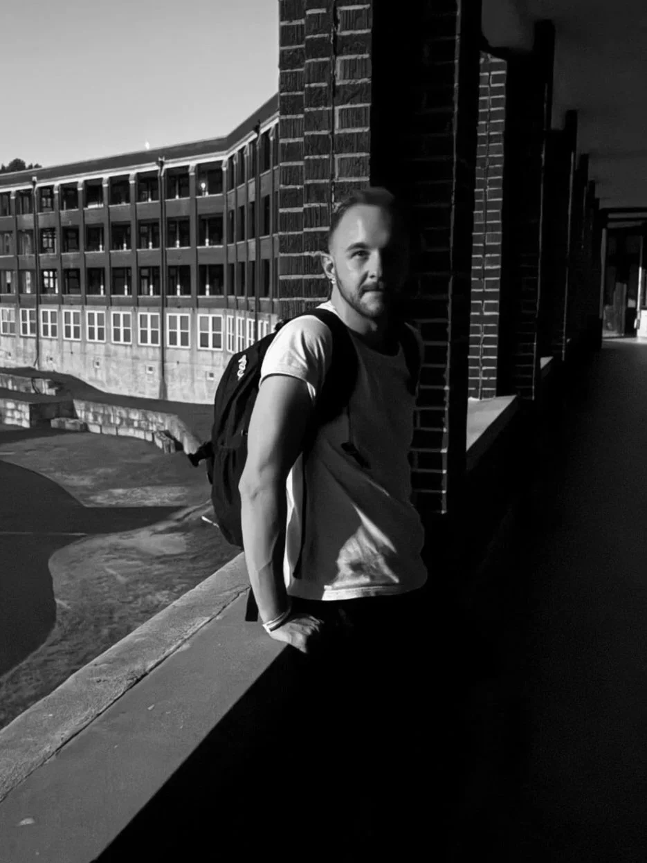 A young man with a backpack standing against a brick wall at night at Waverly Hills Sanitorium, partially illuminated with shadows. Host / Curator of the Oddity Shop Podcast