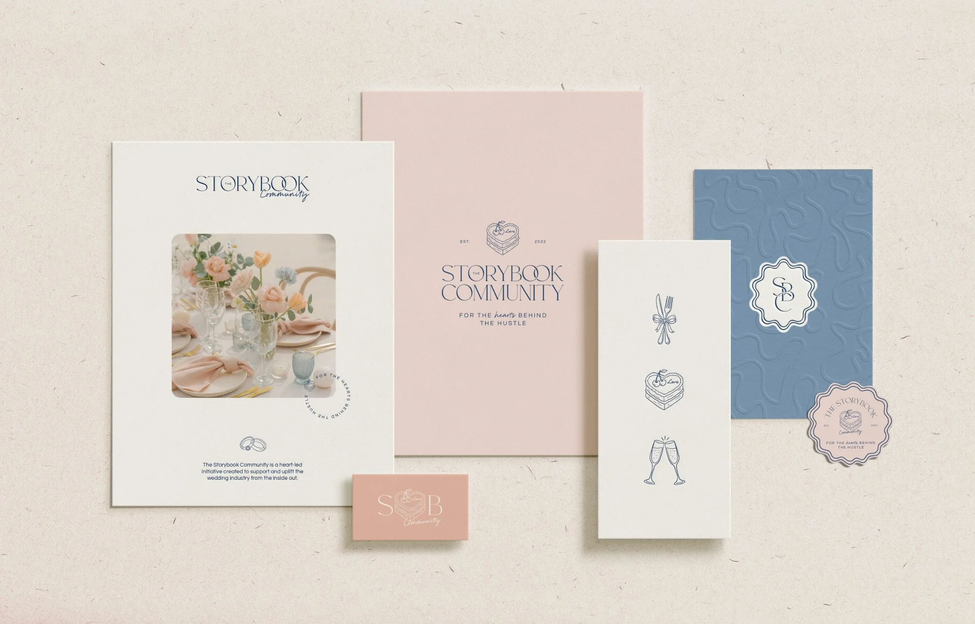 Collection of printed materials including a wedding invitation, branding card, and stationery for the Storybook Community, featuring pastel pink, white, and blue designs with floral and celebratory illustrations.