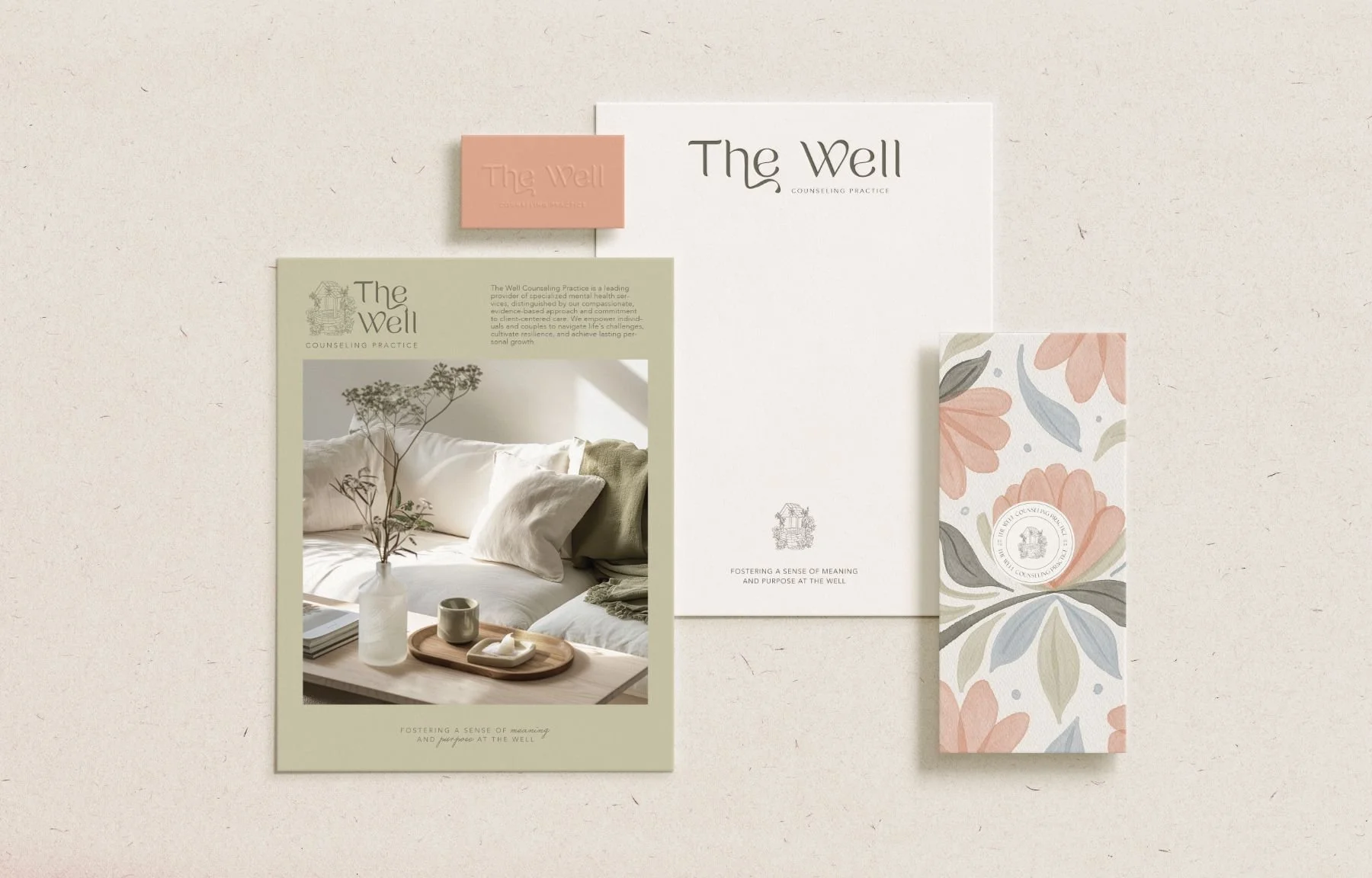 Collection of branding materials for The Well counseling practice, including a small pink business card, a large white letter-sized sheet, a textured navy blue rectangular card with floral design, and a green informational sheet featuring a cozy interior scene with a bed, pillows, and a plant in a vase.