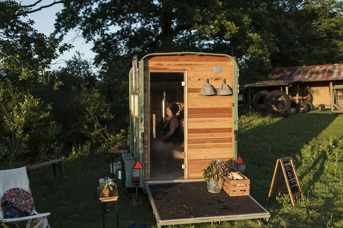A wood fired Saunas in a beautiful natural setting, with someone sitting inside smiling
