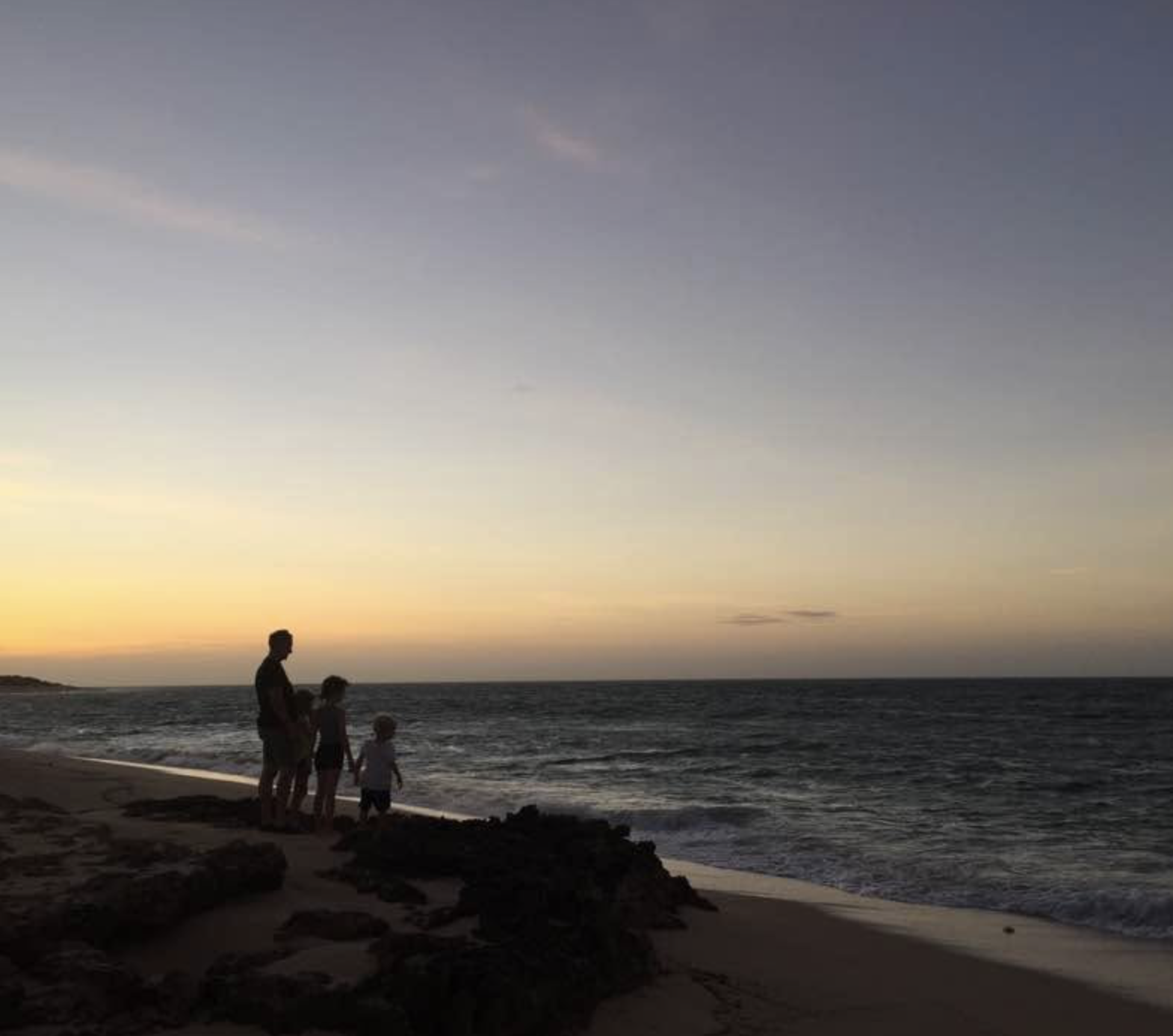 A silhouette of a family walking along the beach at sunset, with the sky blending orange and purple hues, and the ocean waves gently crashing on the shore.
