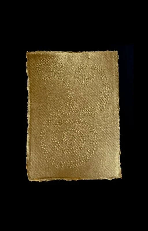 A piece of textured gold paper with spiral patterns, set against a black background.