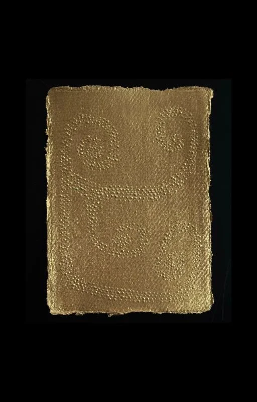 A textured, gold-colored piece of material with spiral and circular patterns created by numerous small bumps, placed on a dark background.