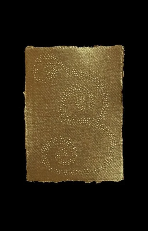 Gold textured card with spiral patterns made of small raised dots, set against a black background.