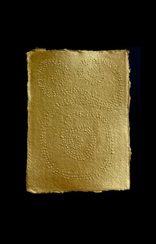 A piece of rough, textured gold-colored paper with braille patterns forming numbers 8 and 9, against a black background.