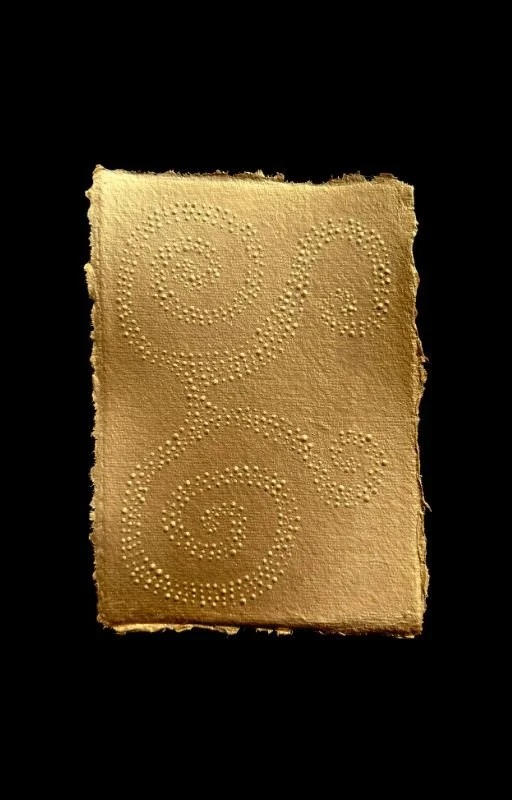 A piece of beige paper with swirling dotted patterns, placed on a black background.