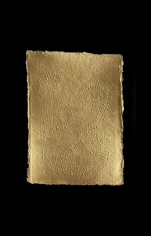 Gold-colored textured card with decorative ampersand made of small dots, against a black background.