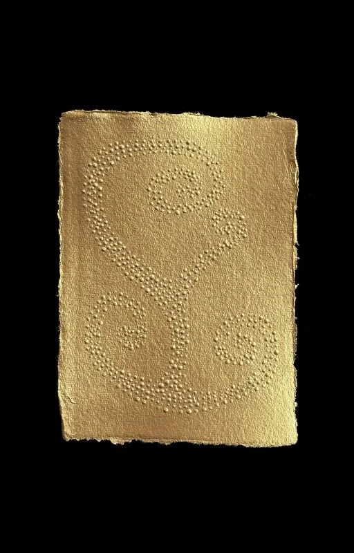A gold-colored textured rectangular card with a decorative swirl and floral pattern made of small holes.