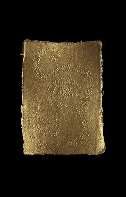 A gold-colored rectangular object with embossed swirls, set against a black background.