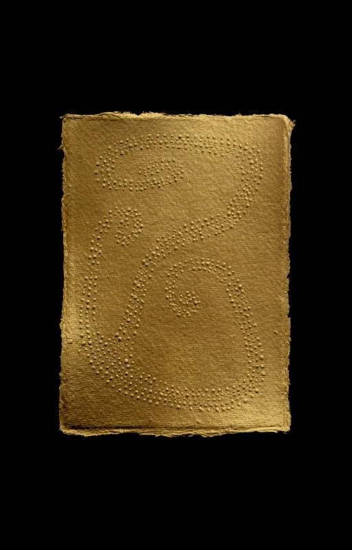 A piece of gold-colored textured paper with raised bumps arranged in decorative patterns on a black background.