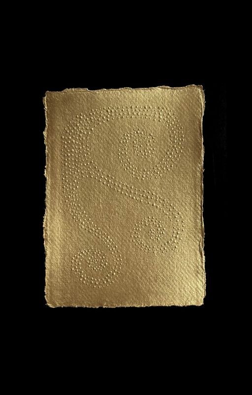 Golden rectangular object with a textured surface and intricate dotted swirl patterns, against a black background.