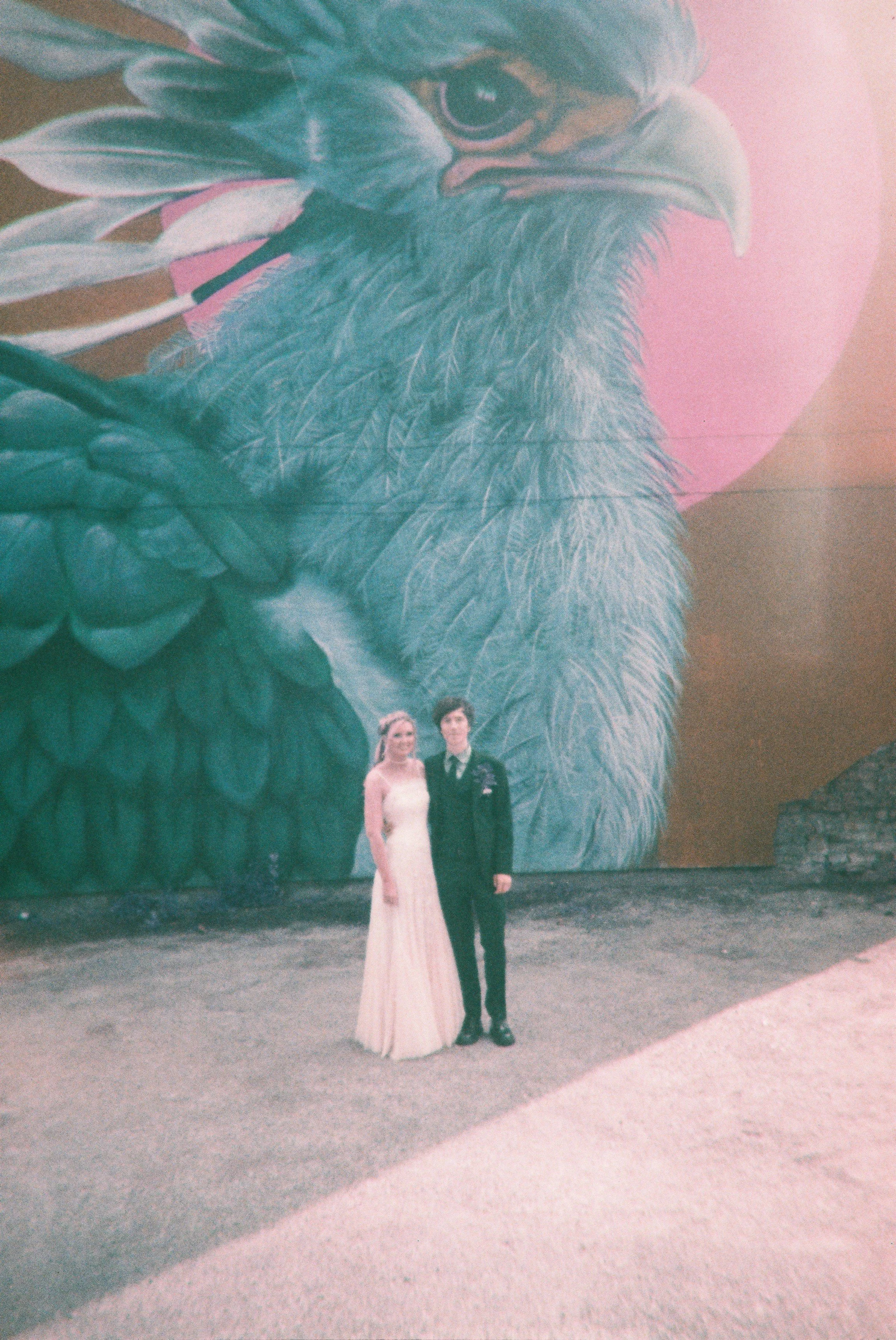 A couple in formal attire standing in front of a large mural of an eagle's head.