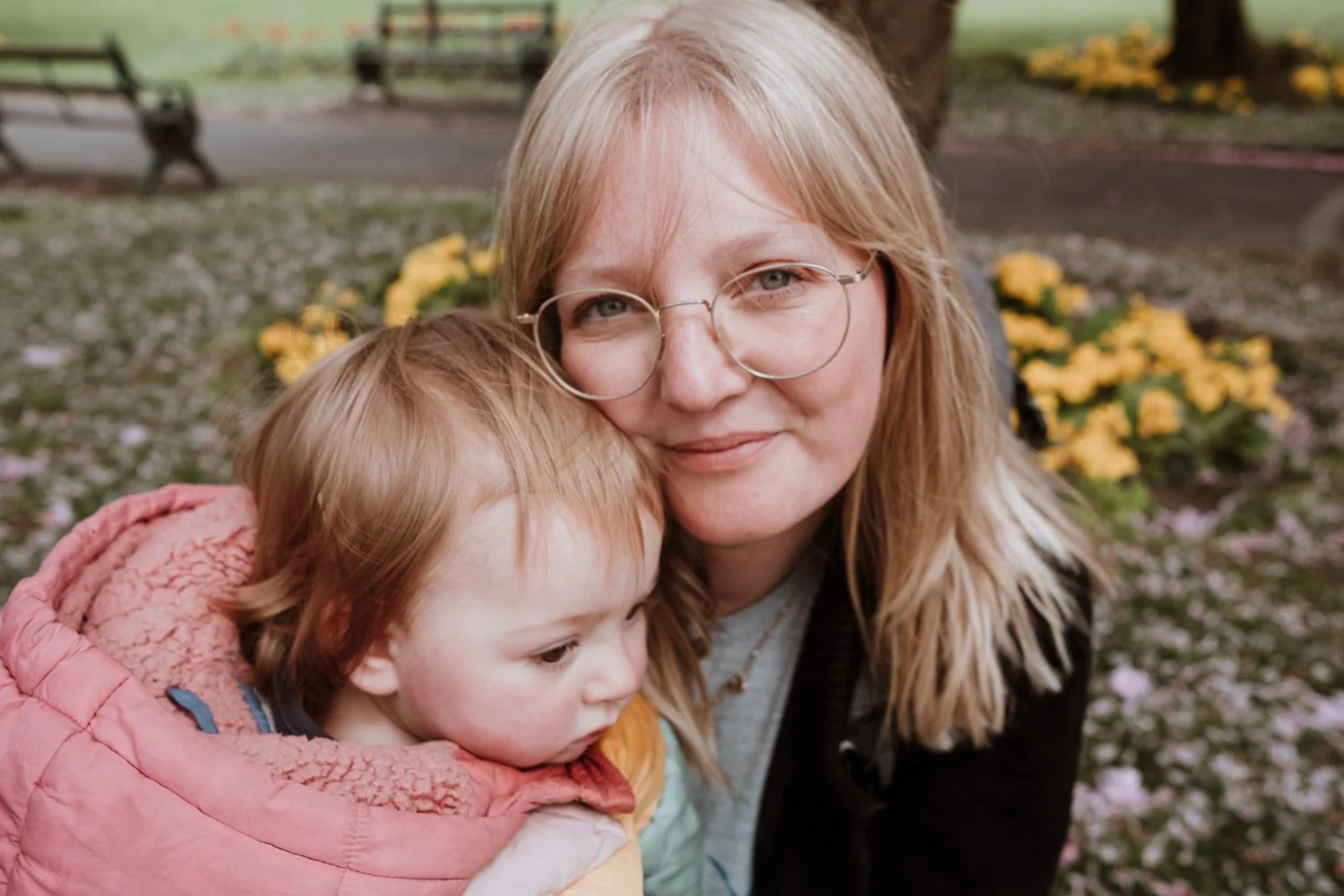 Woman with glasses and child in park with yellow flowers