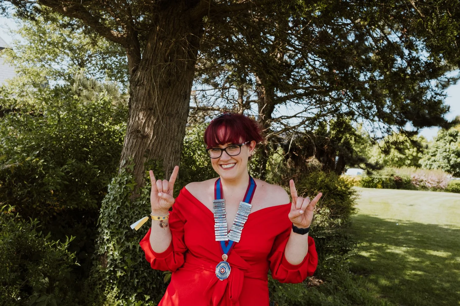 Person in red dress making hand gestures in front of a tree