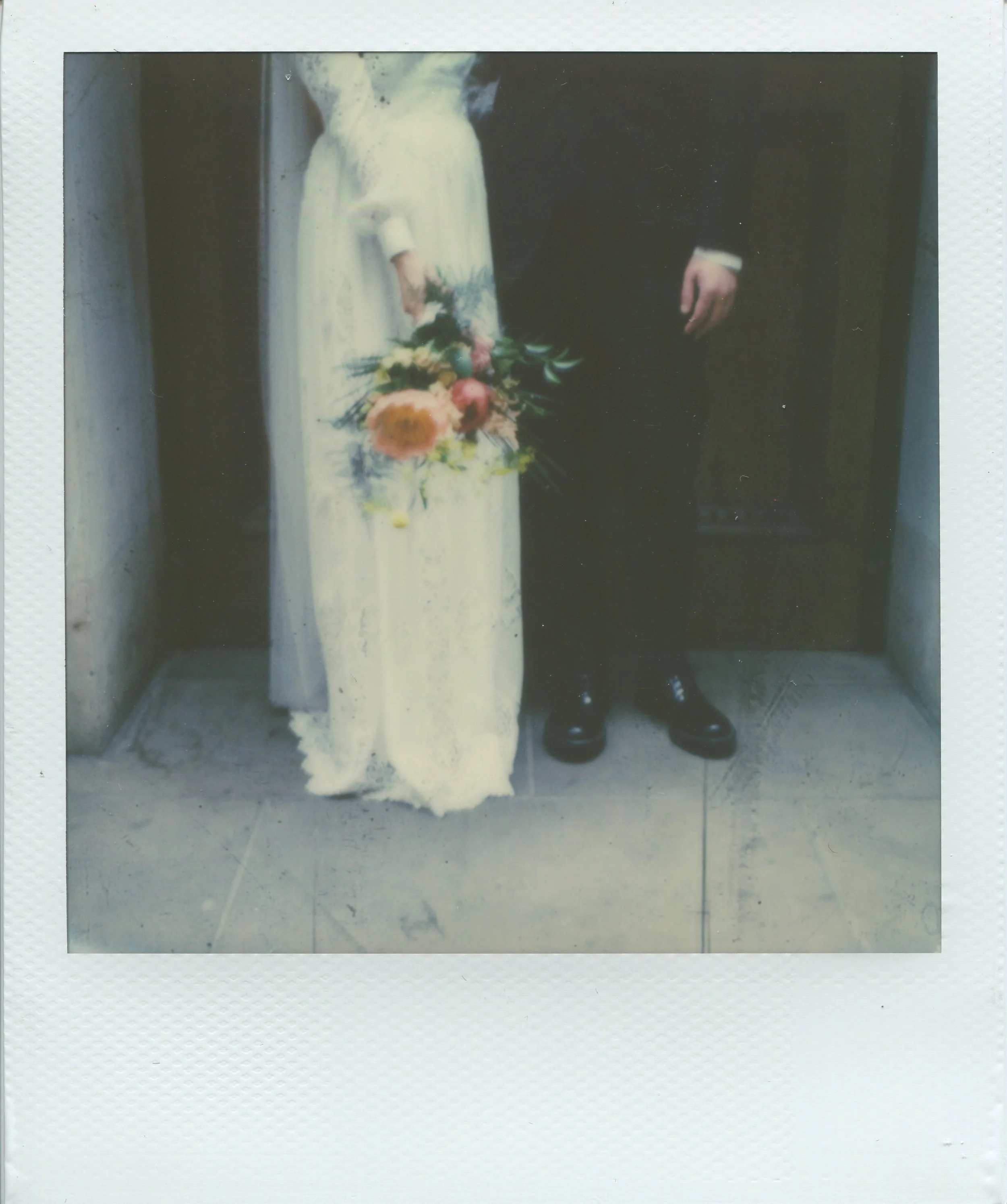 Polaroid of bride and groom standing together, partially visible, with bride holding a bouquet.