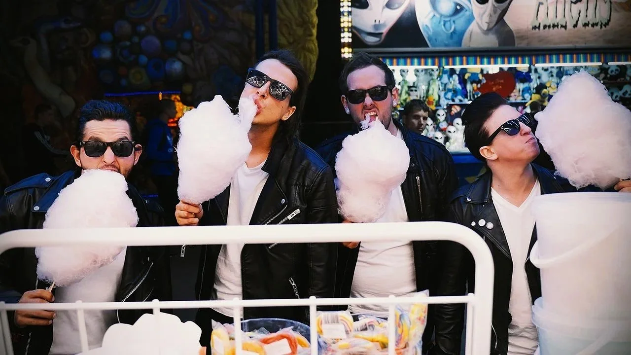 Group of four young adults in leather jackets and sunglasses eating cotton candy at a carnival or fair.