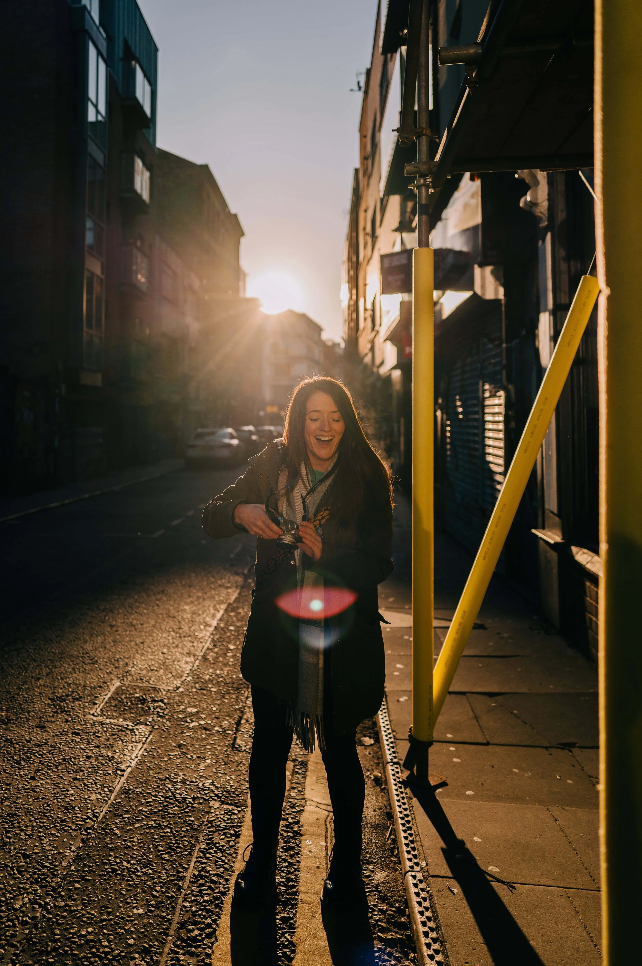 Clare robinson photography laughing whilst holding a camera and back lit in manchester city centre