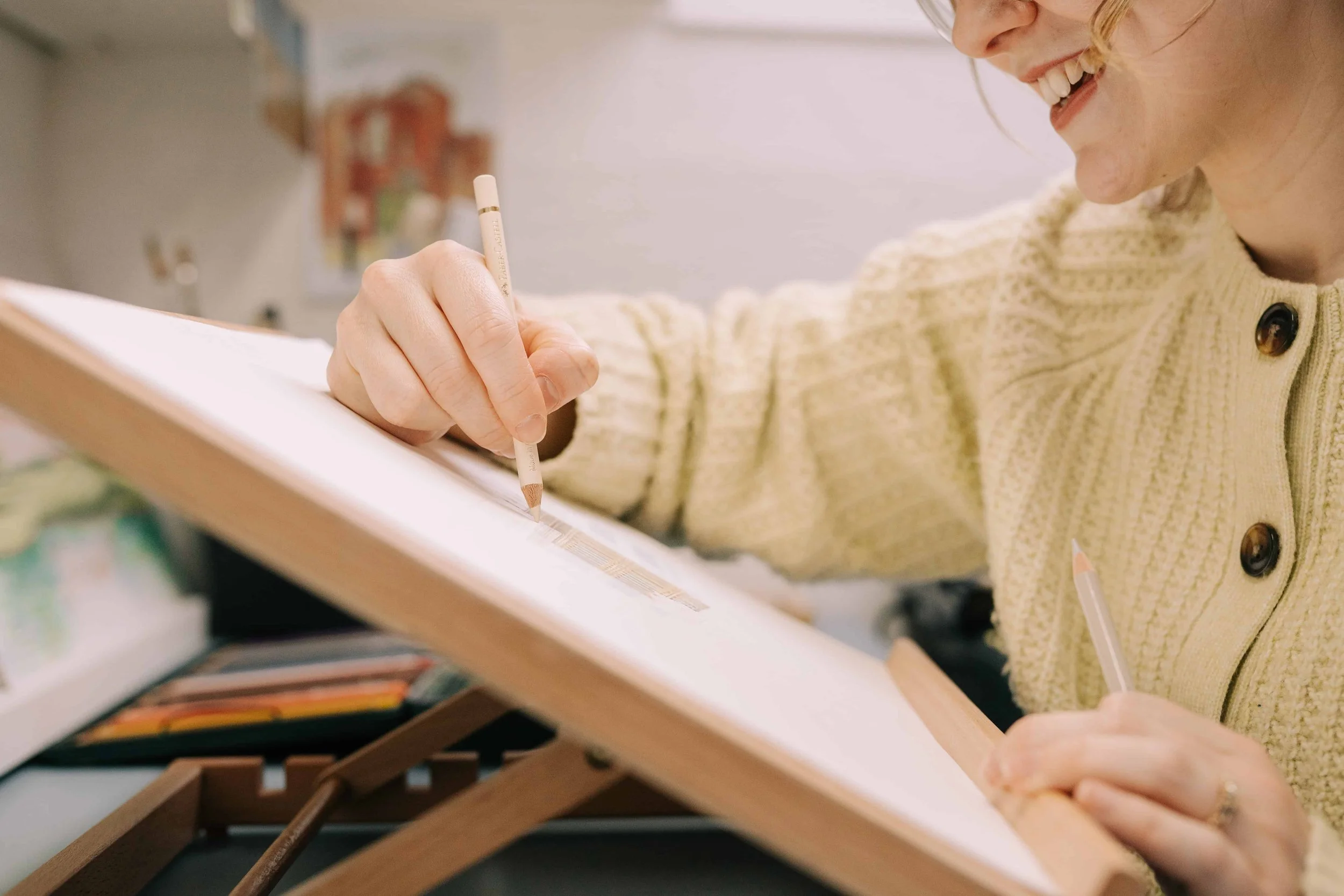 a side on photo of Lydia, fine artist, who is drawing Chatswroth house with coloured pencil