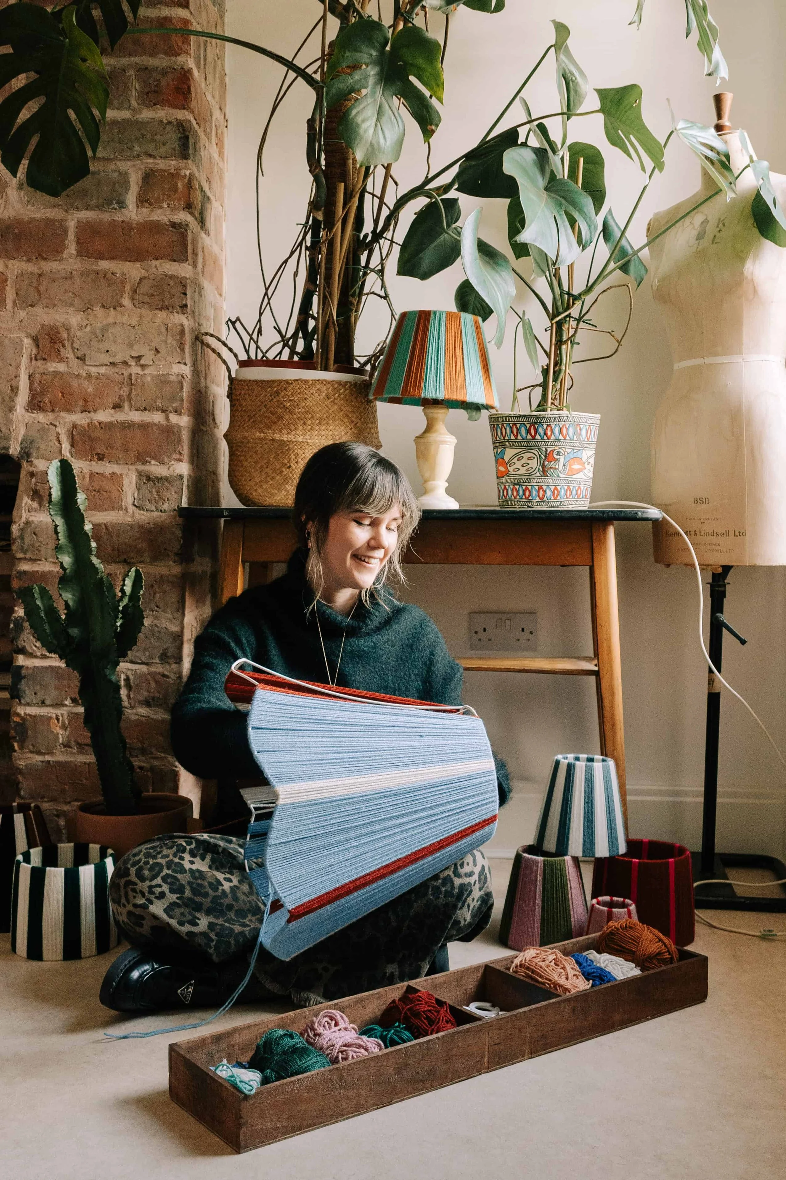 Alice from slide shades sitting on floor hand weaving wool on a large lampshade