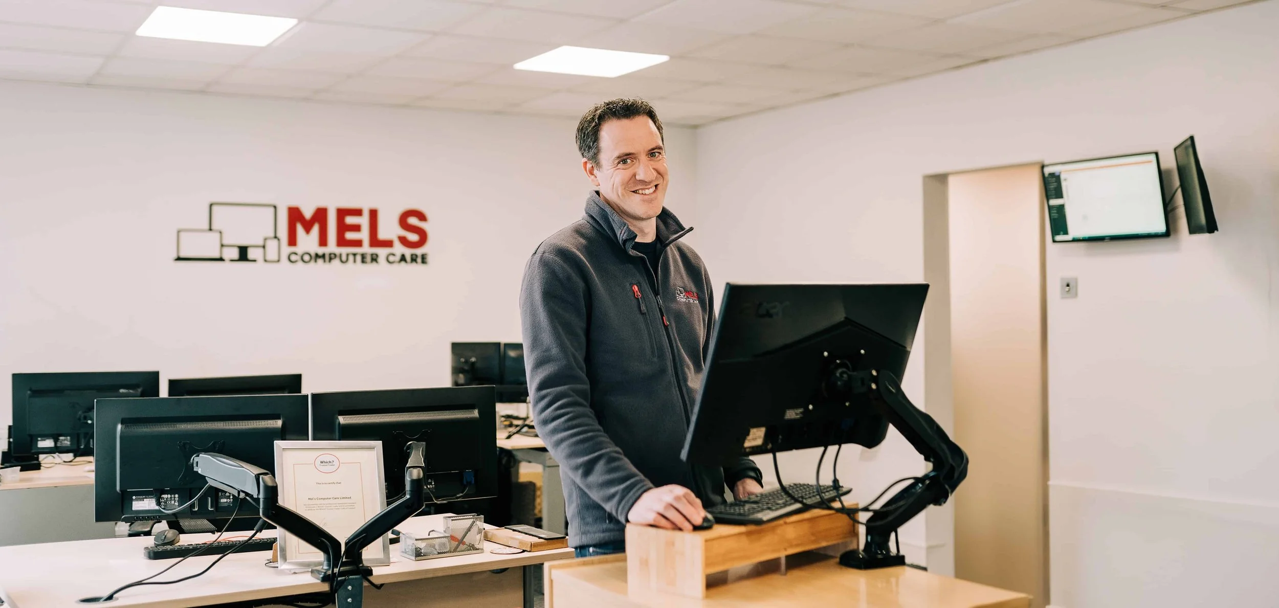 Mel from Mels computer care in Sale moor, stood at his shop counter with a big smile whilst on the computer