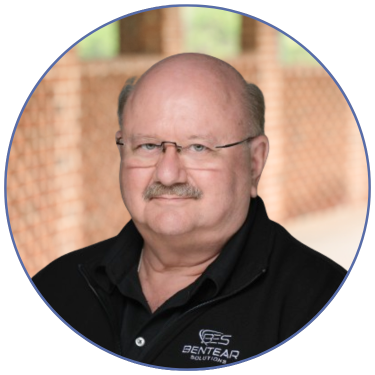 John Degory, a bald man with glasses wearing a black jacket with "BENT EAR SOLUTIONS" logo, standing outdoors.
