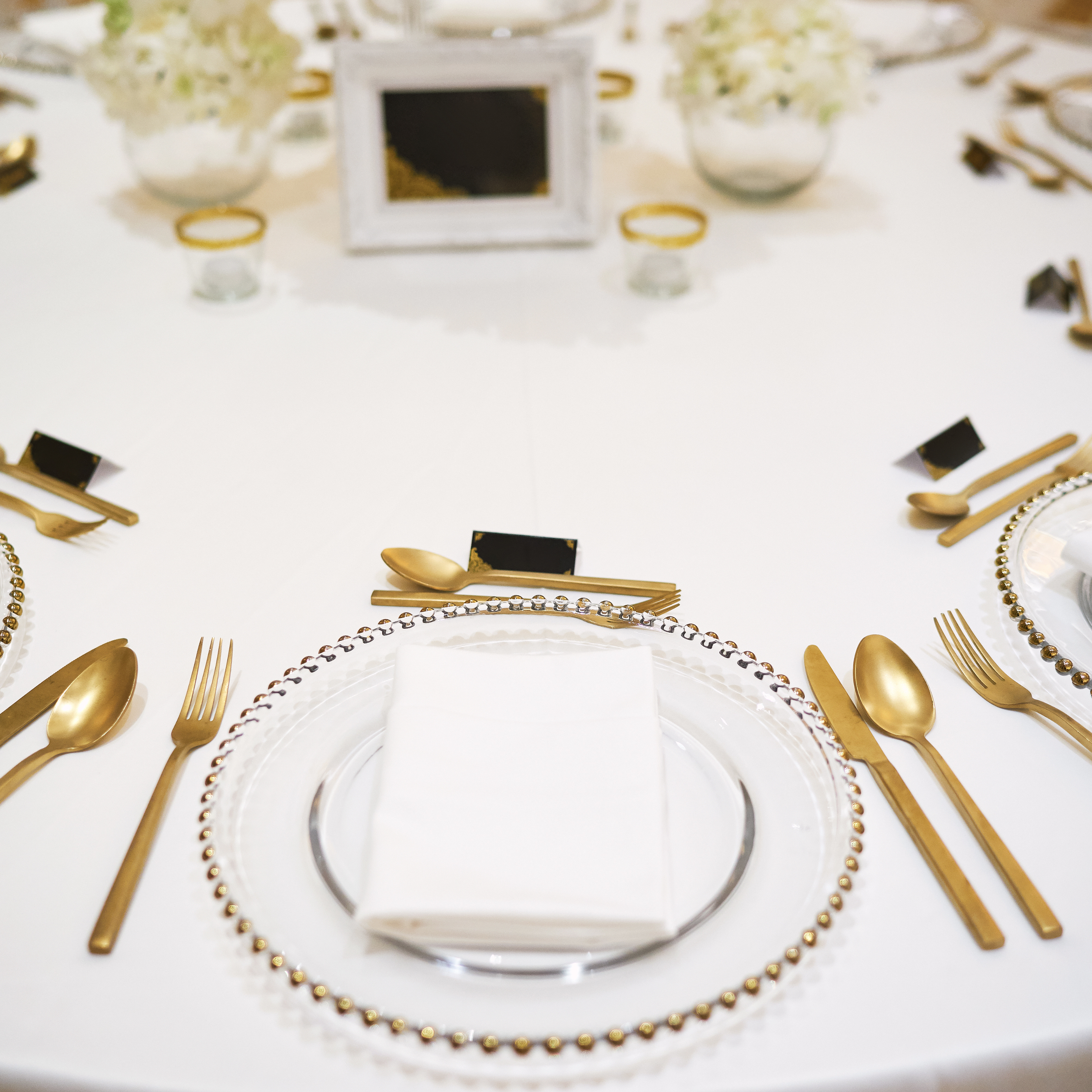 White, black, and gold table setting on white tablecloth at Harbor Brook Hall