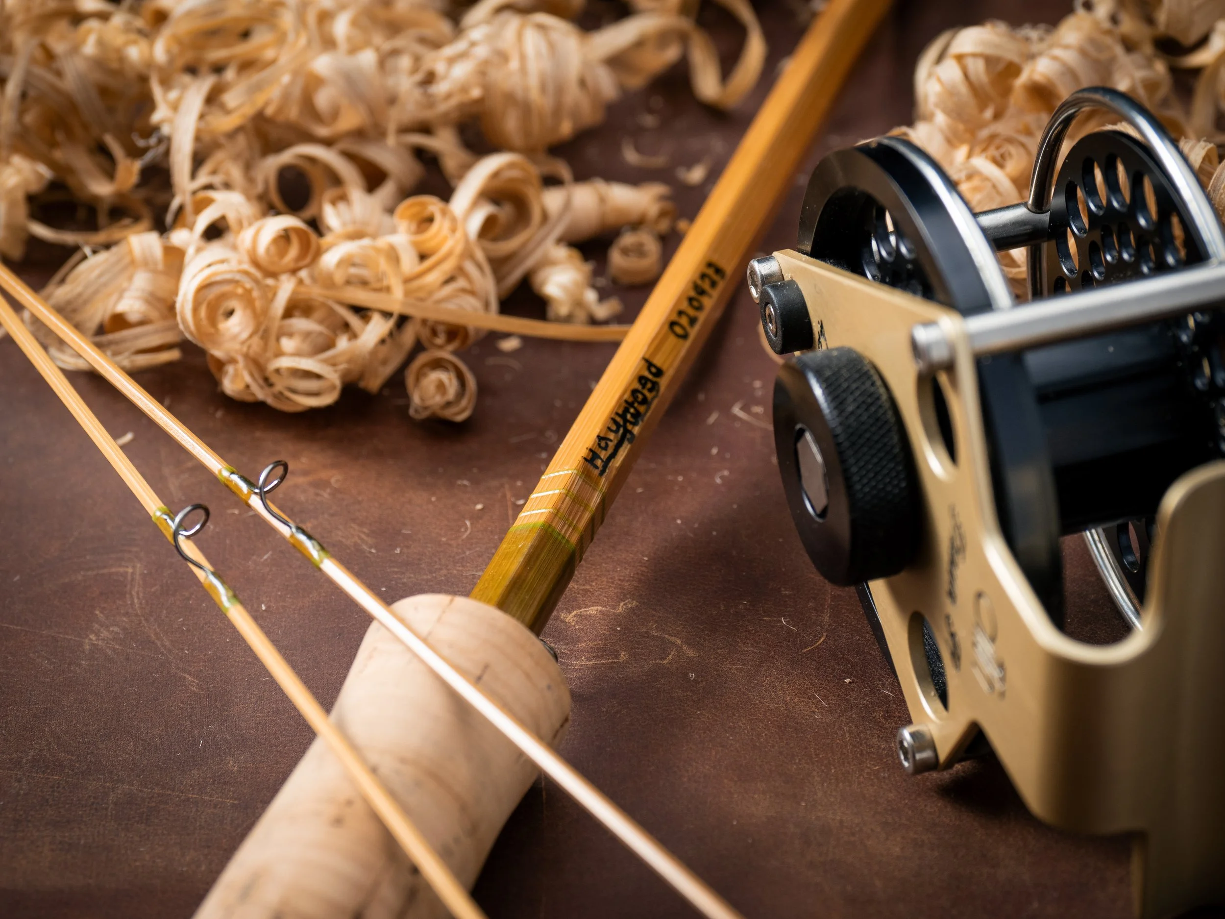 Bamboo rod butt section sitting diagonally with a fly reel and bamboo shavings on either side.