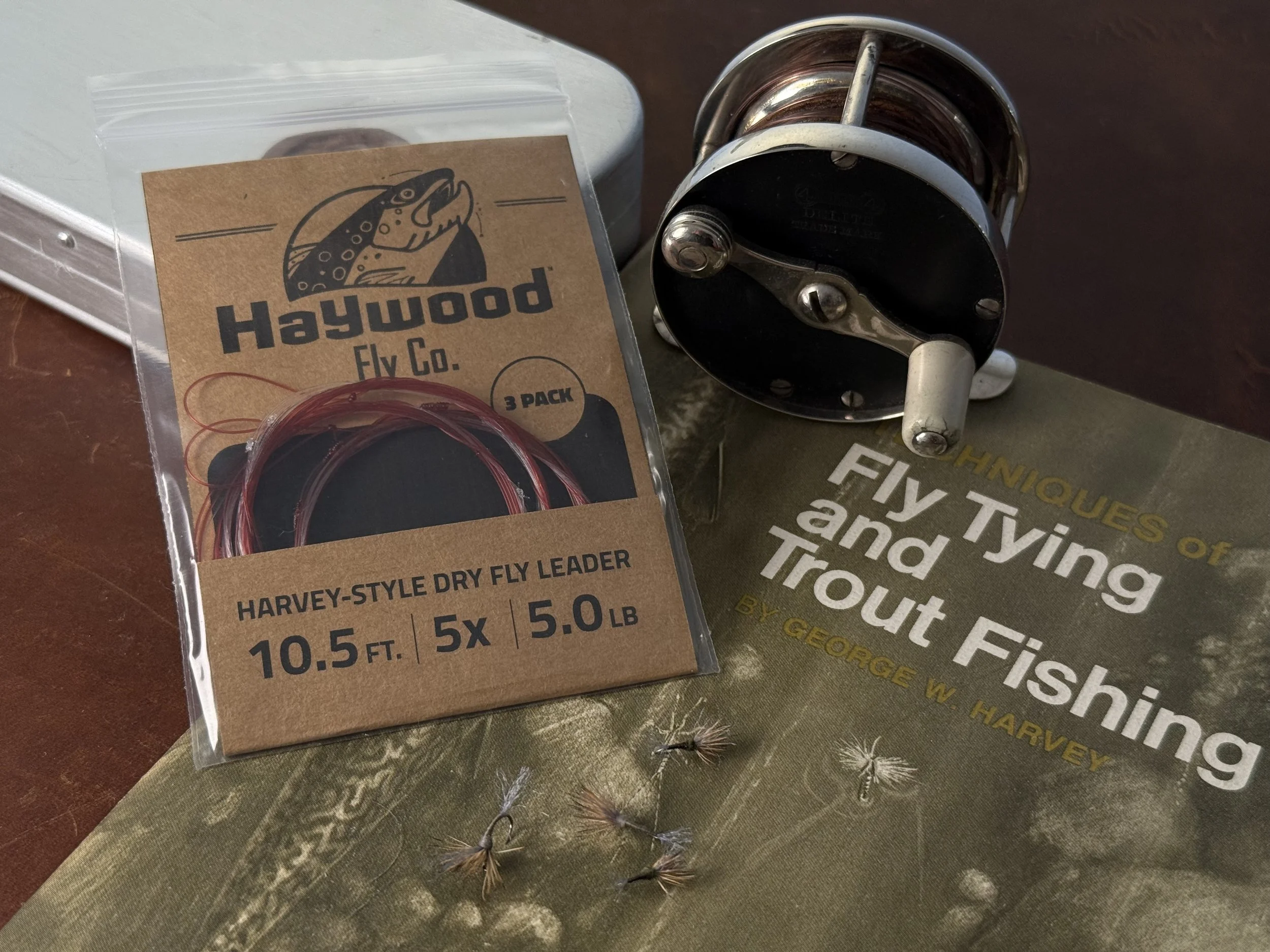 Package of fly fishing leaders sitting on a book next to an antique fly reel.