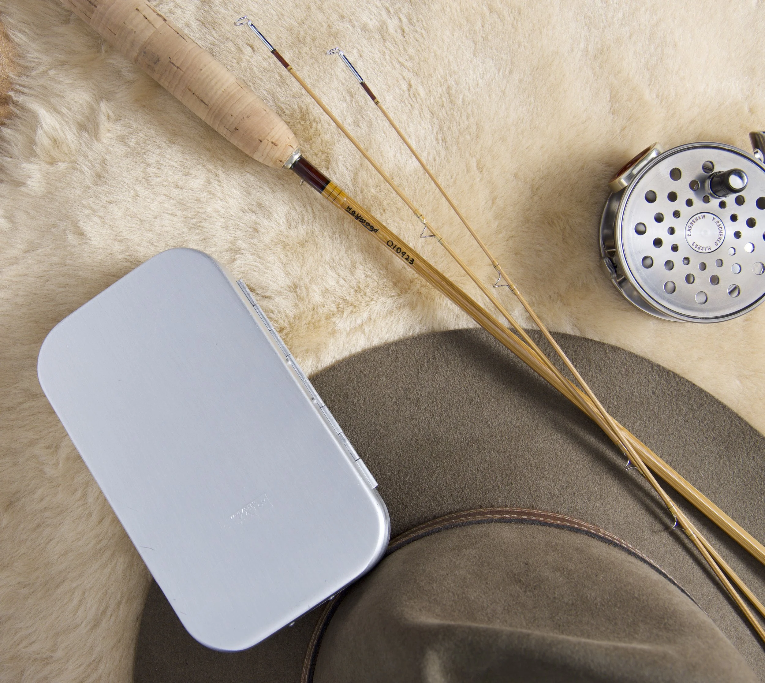 Bamboo fly rod, felt hat, fly reel and aluminum fly box on shearling.