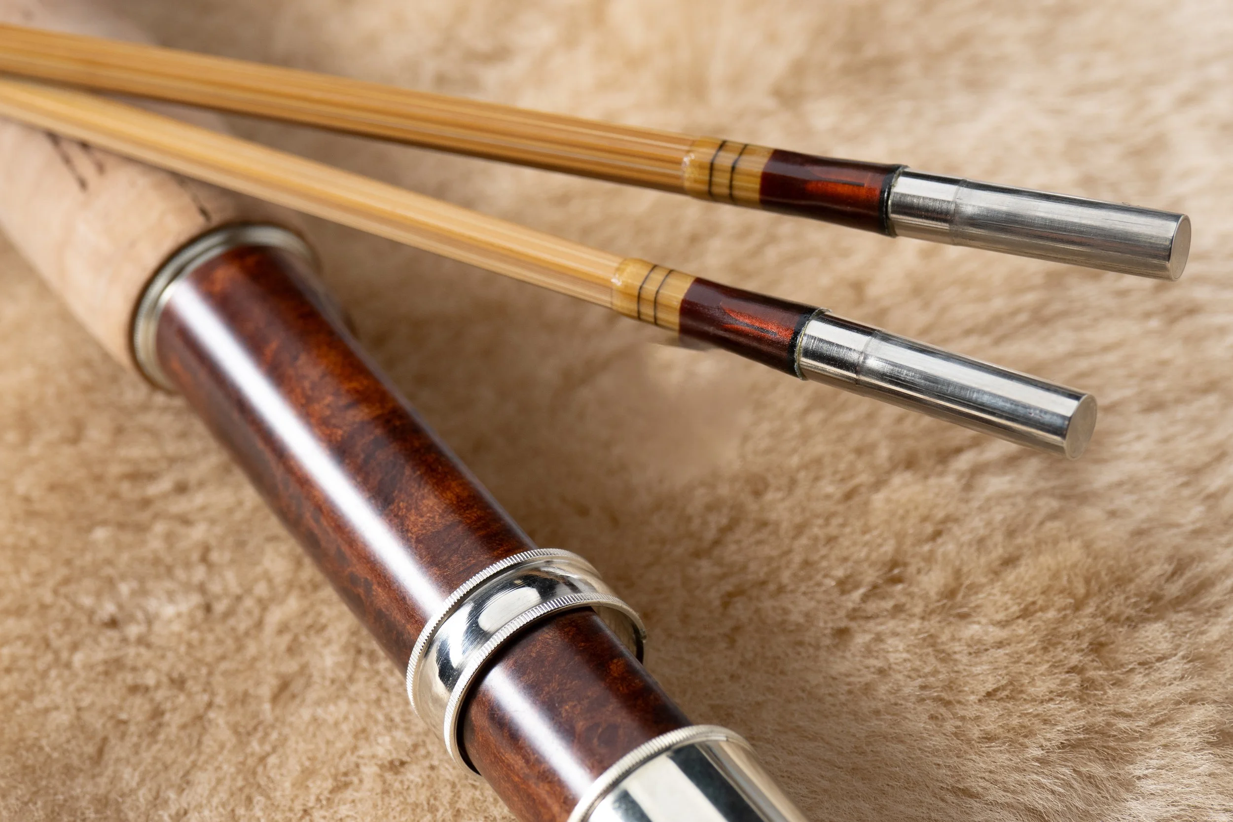 Bamboo fly rod section featuring brown wraps and redwood burl reel seat sitting on shearling.
