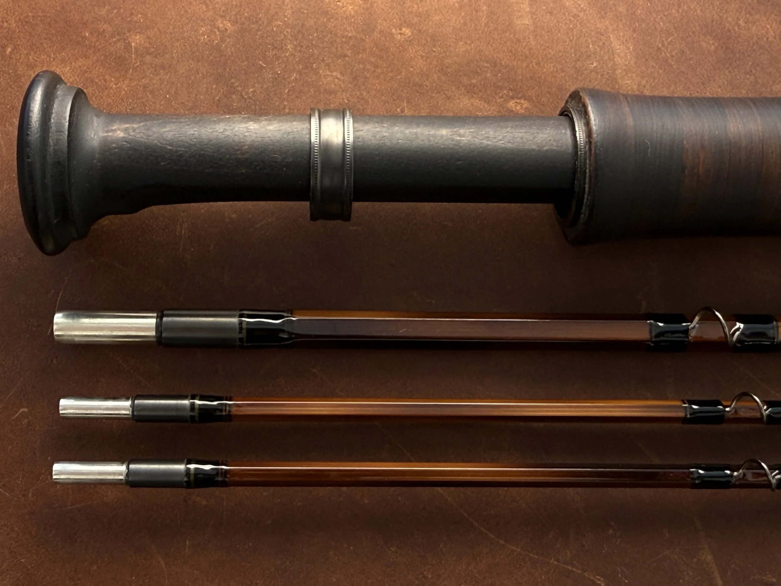 Heavily flamed fly rod sections with machined metal ferrule fittings below a butt section featuring a custom turned and ebonized cherry reel seat.