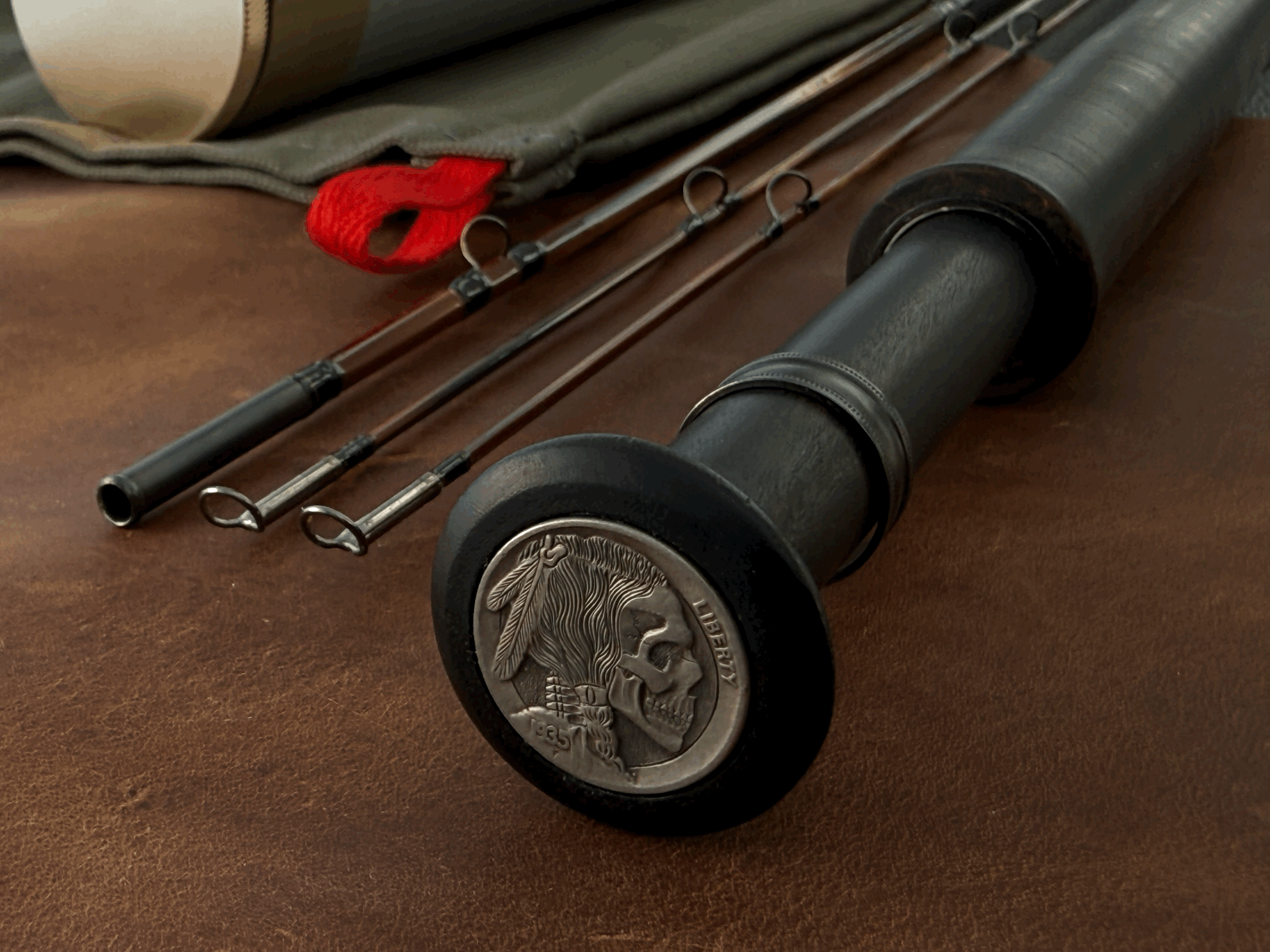 Reel seat of rod with skull engraved in 1935 Indian Head nickel. Tip and mid sections next laying beside.