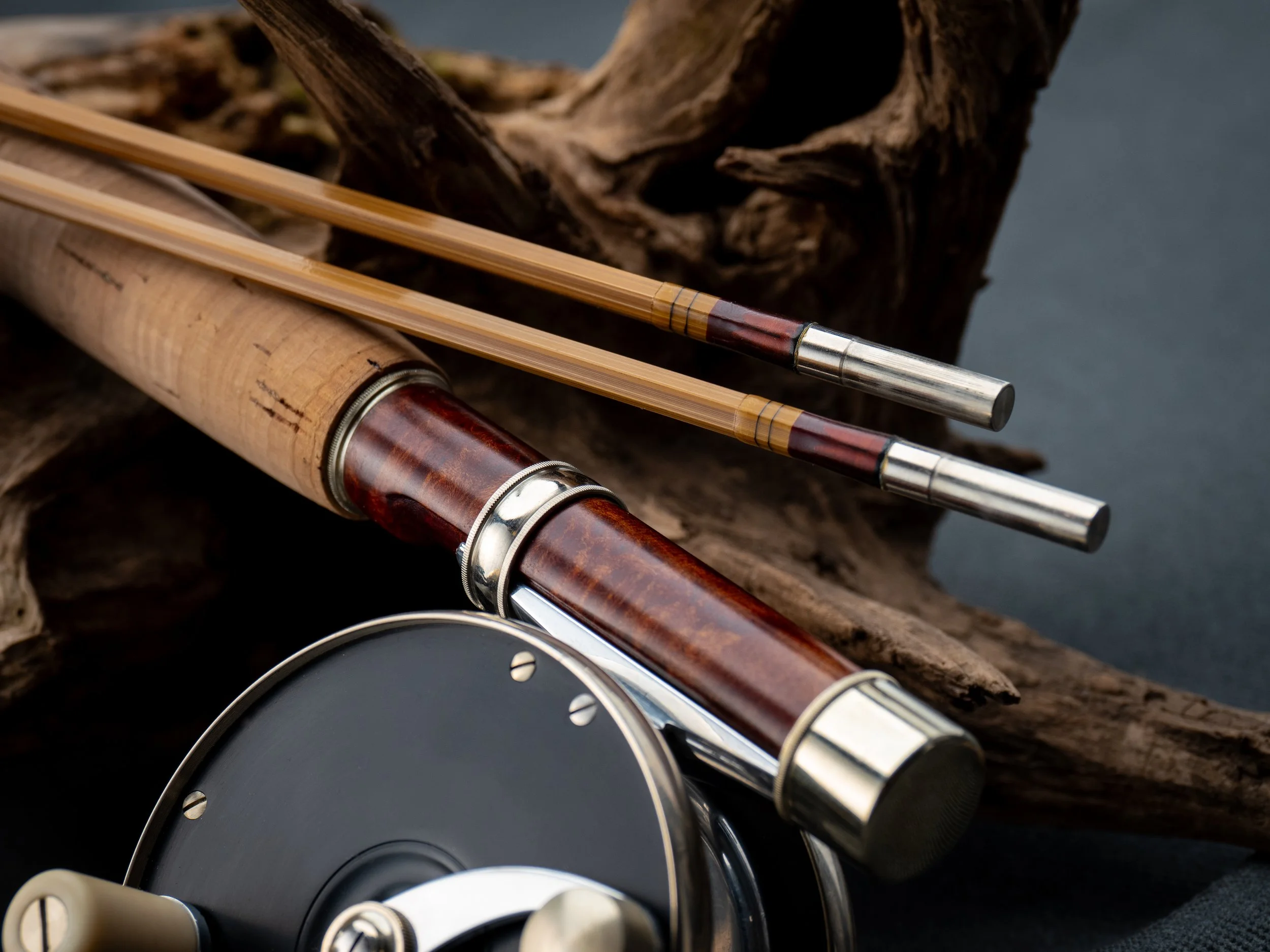 Bamboo rod butt section with classic fly reel and two tip sections sitting on driftwood.