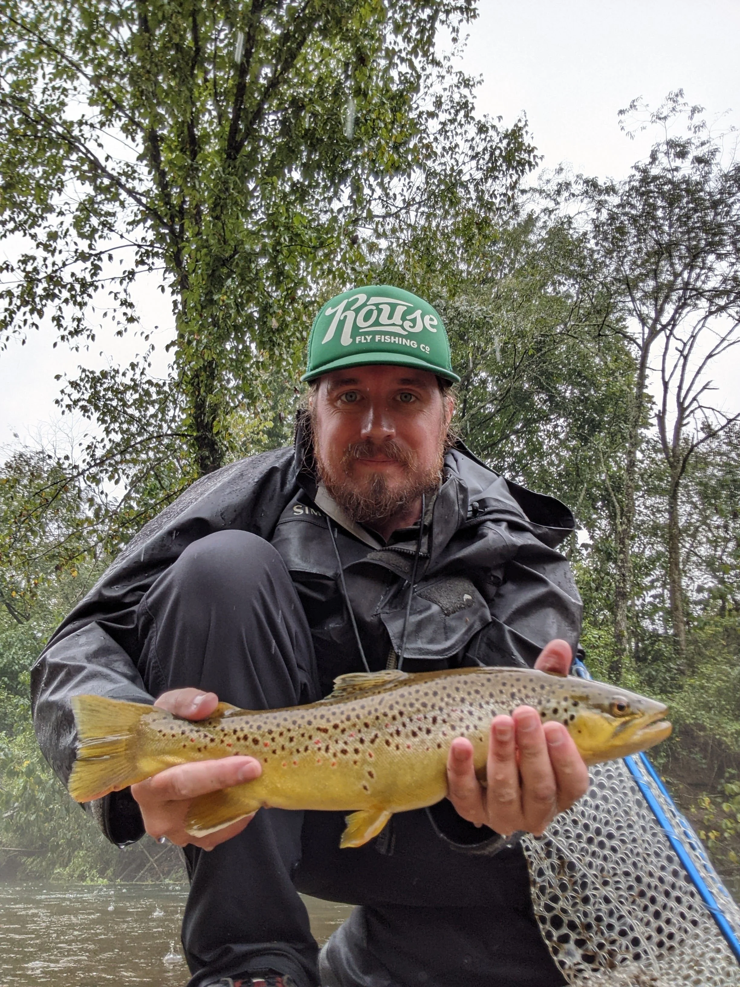 40-year-old man kneeling and holding brown trout in the rain.